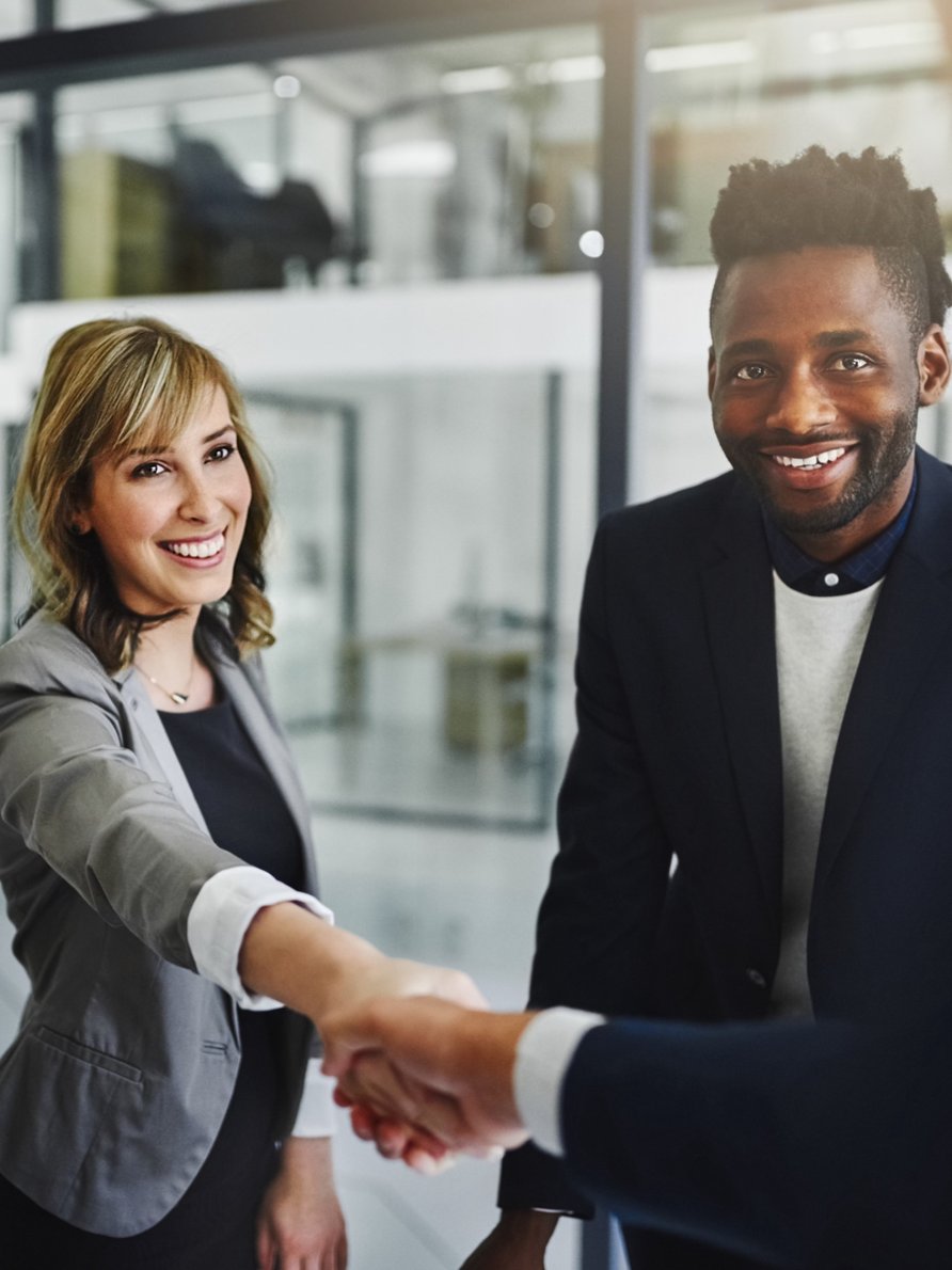 Man and woman in business attire shaking a hand and smiling